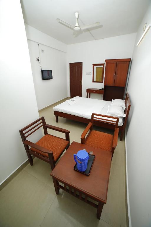 a room with a bed and a table and chairs at Kairali Tourist Home in Guruvāyūr