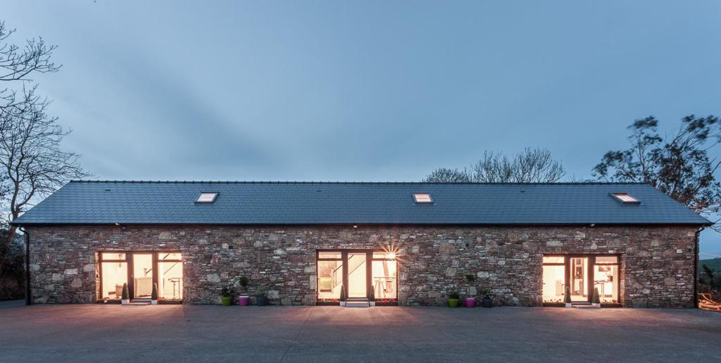 a stone building with doors and a black roof at Curragh House Lodges in Kinsale
