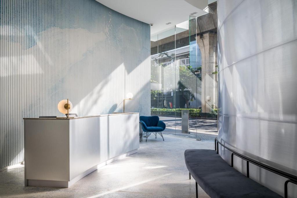 A bright hotel lobby reception area with a desk, lounge chair, and street-facing glass entrance.