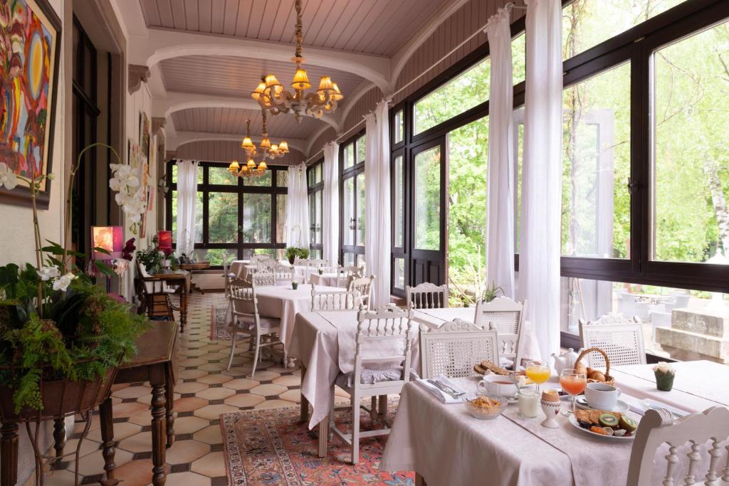 um restaurante com mesas e cadeiras brancas e janelas em Domaine de Beaupré - Hotel The Originals Relais em Guebwiller