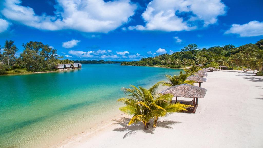 Holiday Inn Resort Vanuatu, an IHG Hotel في بورت فيلا: شاطئ به العديد من مظلات القش والماء