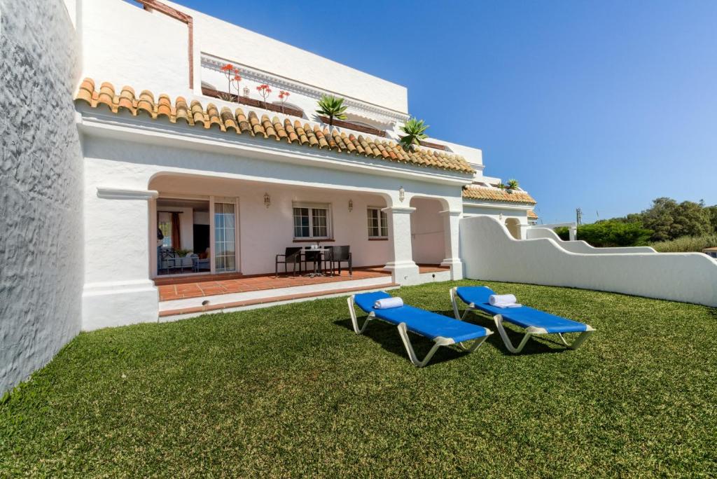 a yard with two blue chairs and a house at Villas Flamenco Beach Conil in Conil de la Frontera