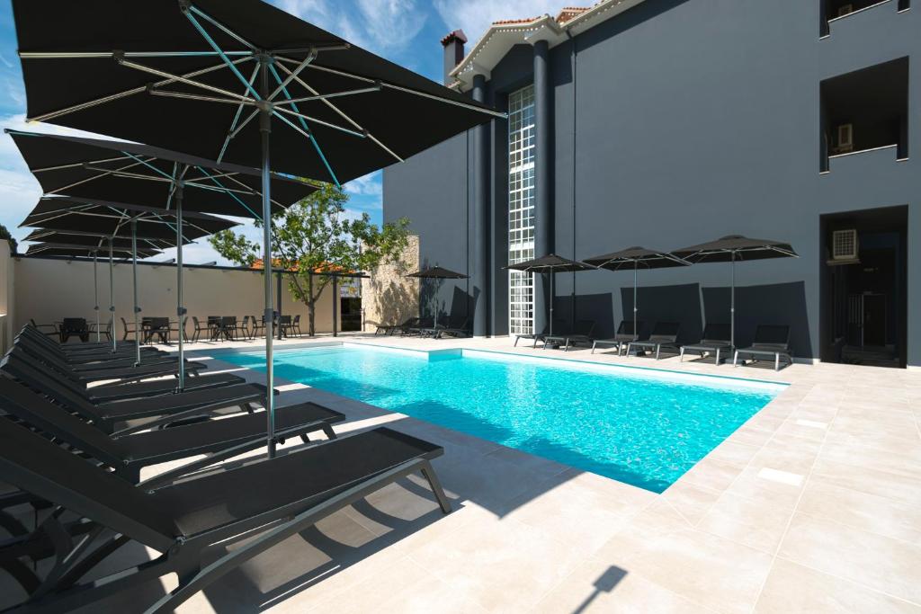 a pool with chairs and umbrellas next to a building at Hotel Cabecinho in Anadia