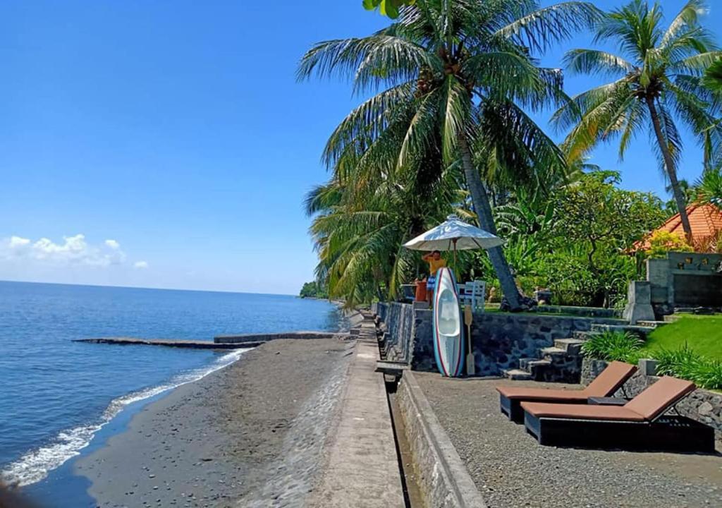 a beach with chairs and an umbrella and a surfboard at Mojito Beach Villas in Kubutambahan
