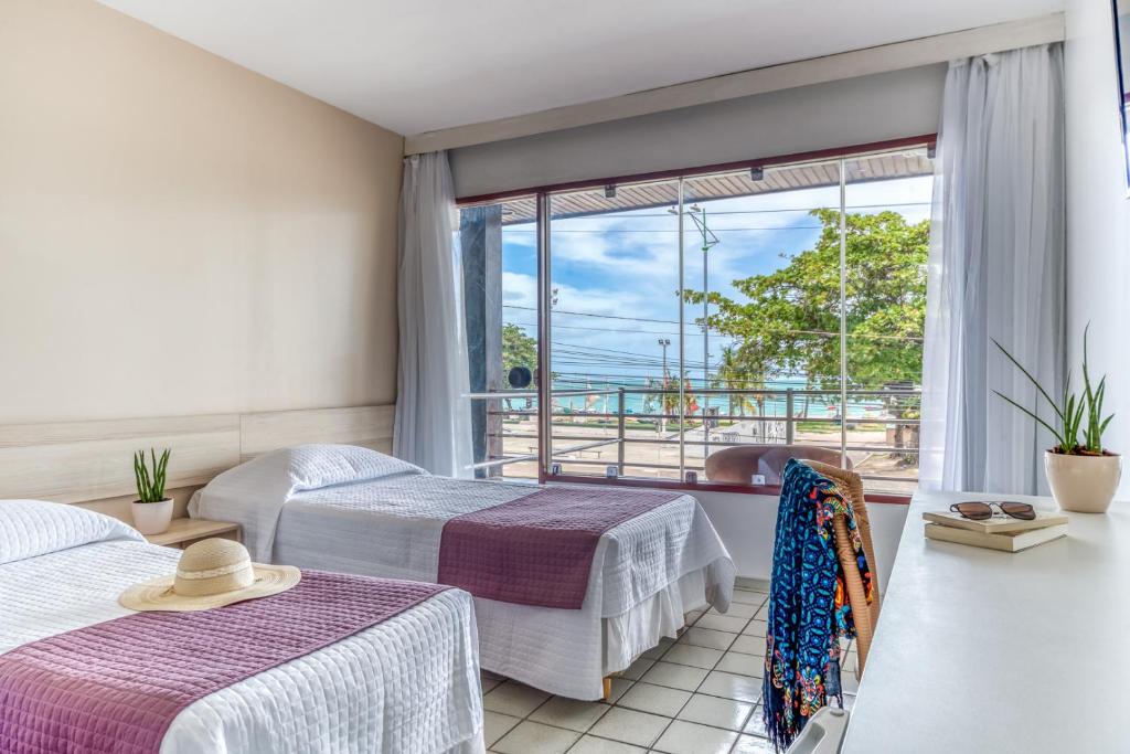 a hotel room with two beds and a large window at Hotel Praia Bonita Pajuçara in Maceió