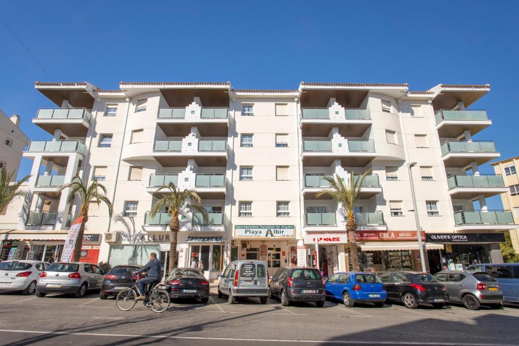a tall white building with cars parked in a parking lot at Apartamentos BCL Playa Albir in Albir