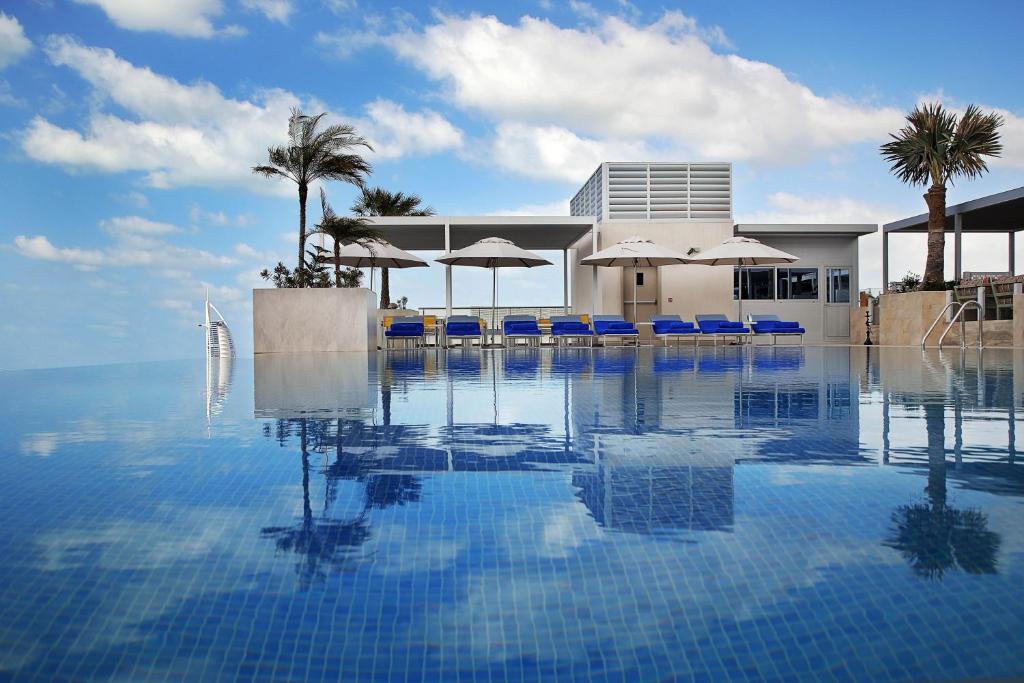 杜拜的住宿－Grand Cosmopolitan Hotel，一个带蓝色椅子和遮阳伞的游泳池