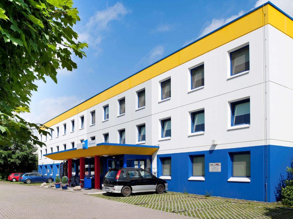 um edifício branco e azul com um carro estacionado em frente em ibis budget Muenchen Putzbrunn em Putzbrunn