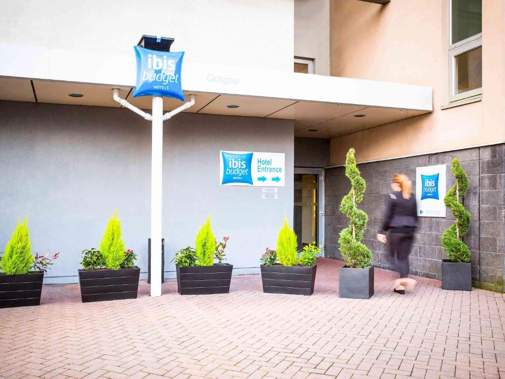 a person walking in front of a building with plants at ibis budget Glasgow in Glasgow