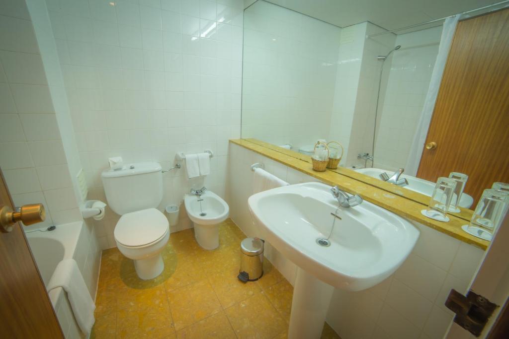 a bathroom with a sink and a toilet and a mirror at Hotel Porto Santo & Spa in Porto Santo