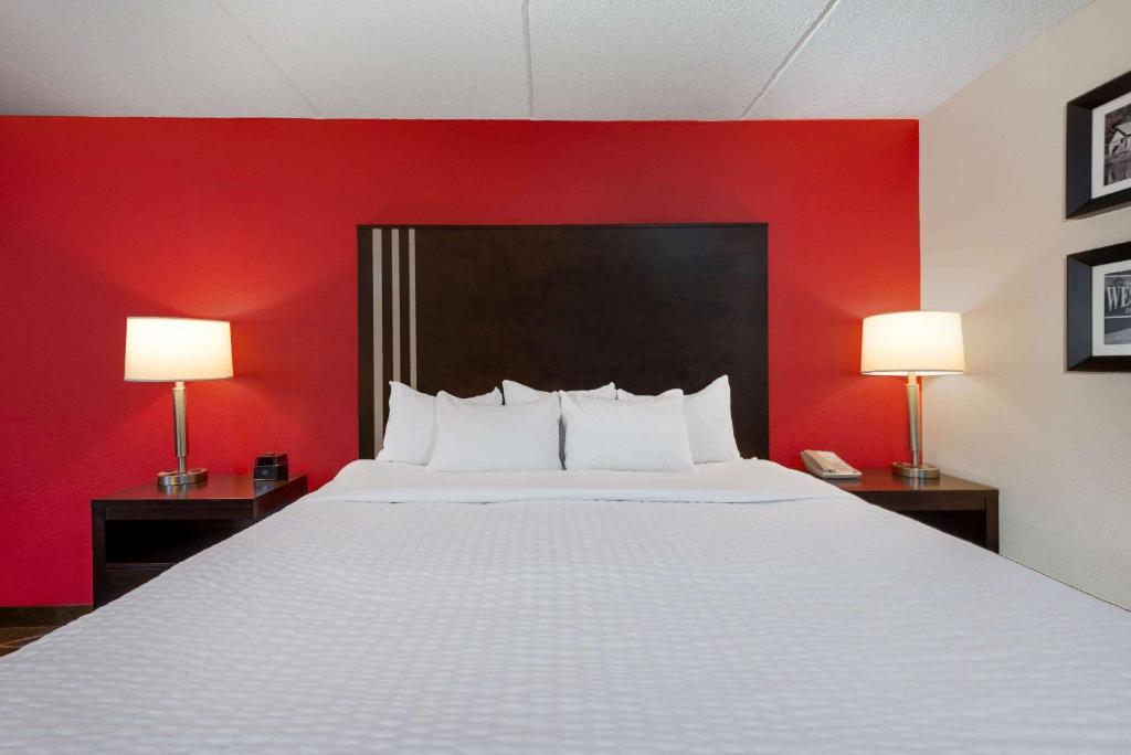 a bed in a room with a red wall and two lamps at La Quinta Inn & Suites - New River Gorge National Park in Summersville