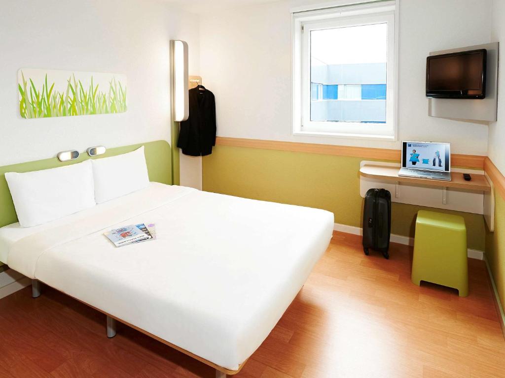 Un dormitorio con una cama blanca y un ordenador portátil en un escritorio. en Ibis Budget Valencia Aeropuerto, en Manises