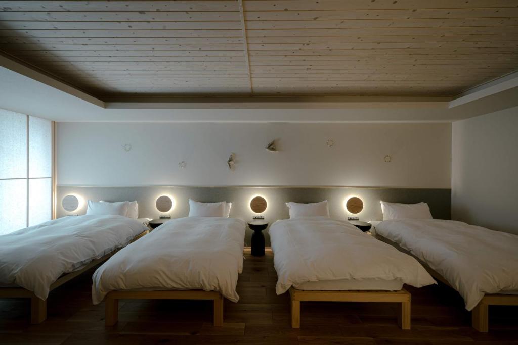three beds in a room with white sheets and lights at so, KANAZAWA in Kanazawa