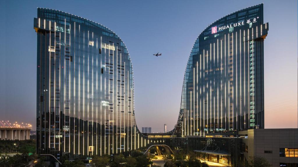廈門市にあるHUALUXE Xiamen Haicang Habour View - An IHG Hotelの夜の街中の高いガラス張りの建物2棟