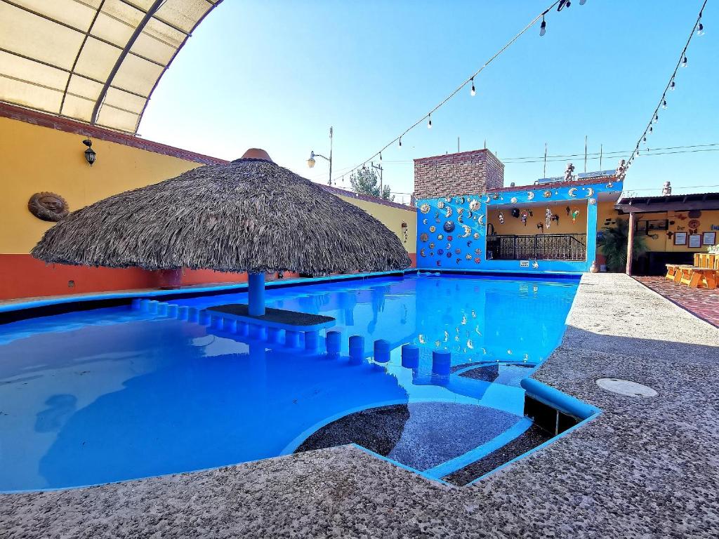 a swimming pool with a straw umbrella next to a building at Hotel La Estancia in Río Verde