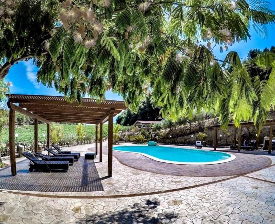 a swimming pool with a pavilion and chairs and a tree at Agriturismo Tenute Pispisa Segesta in Calatafimi
