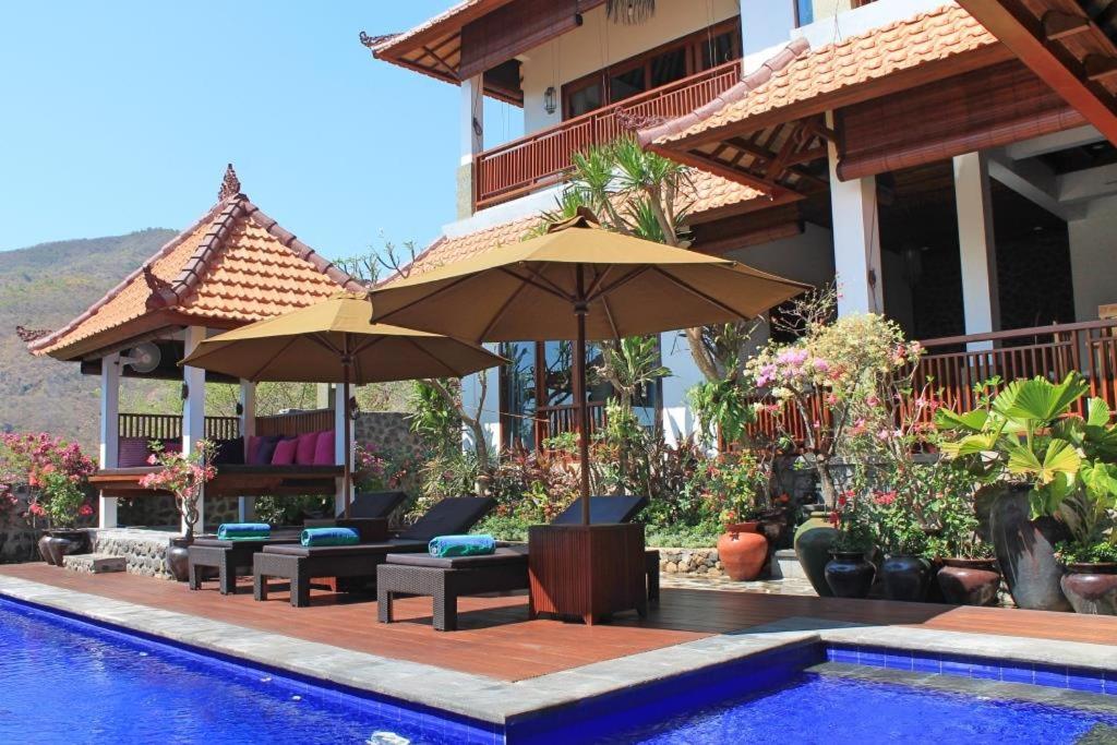einen Pool mit Sonnenschirmen und Stühlen neben einem Haus in der Unterkunft Villa Bukit Malas 4, 4 Bedroom Villa and Pool in Ambat