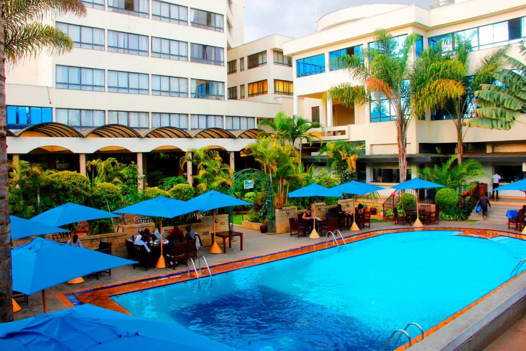 une piscine avec des parasols bleus en face d'un hôtel dans l'établissement Merica Hotel, à Nakuru