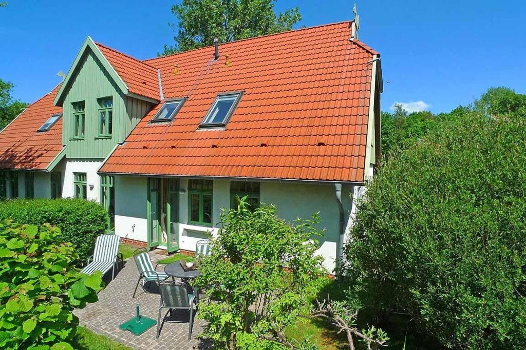 a green house with an orange roof and chairs at Ferienhaussiedlung Strandperlen Sanddornhof 3d (Typ I) in Wustrow