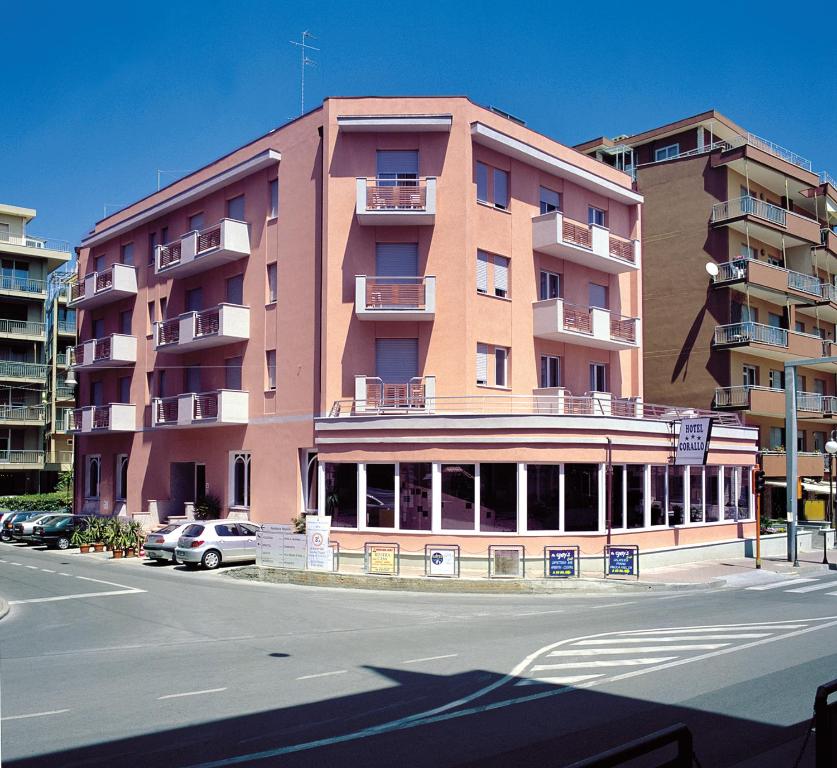a large pink building with cars parked in front of it at Hotel Corallo in Pietra Ligure