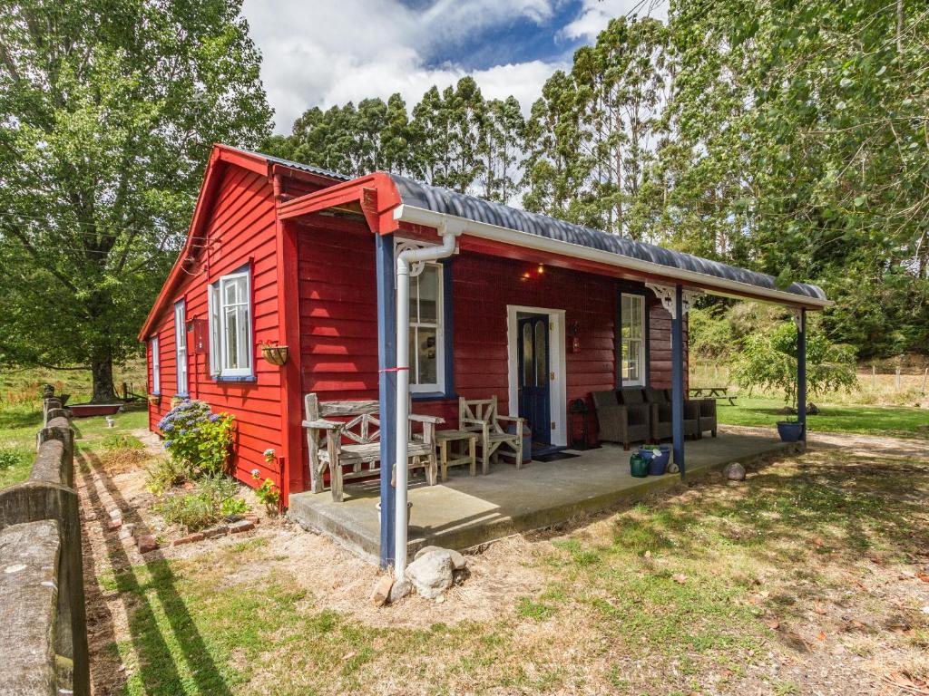 une petite maison rouge avec une terrasse couverte dans l'établissement The Red Rooster Cottage, à Raurimu Spiral