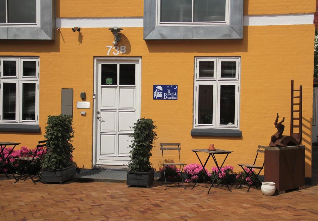 żółty budynek z białymi drzwiami, stołami i krzesłami w obiekcie Odense City B&B w mieście Odense
