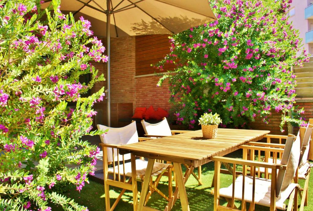 una mesa de madera y sillas en un jardín con flores rosas en Apartamento Laurel, en Lloret de Mar