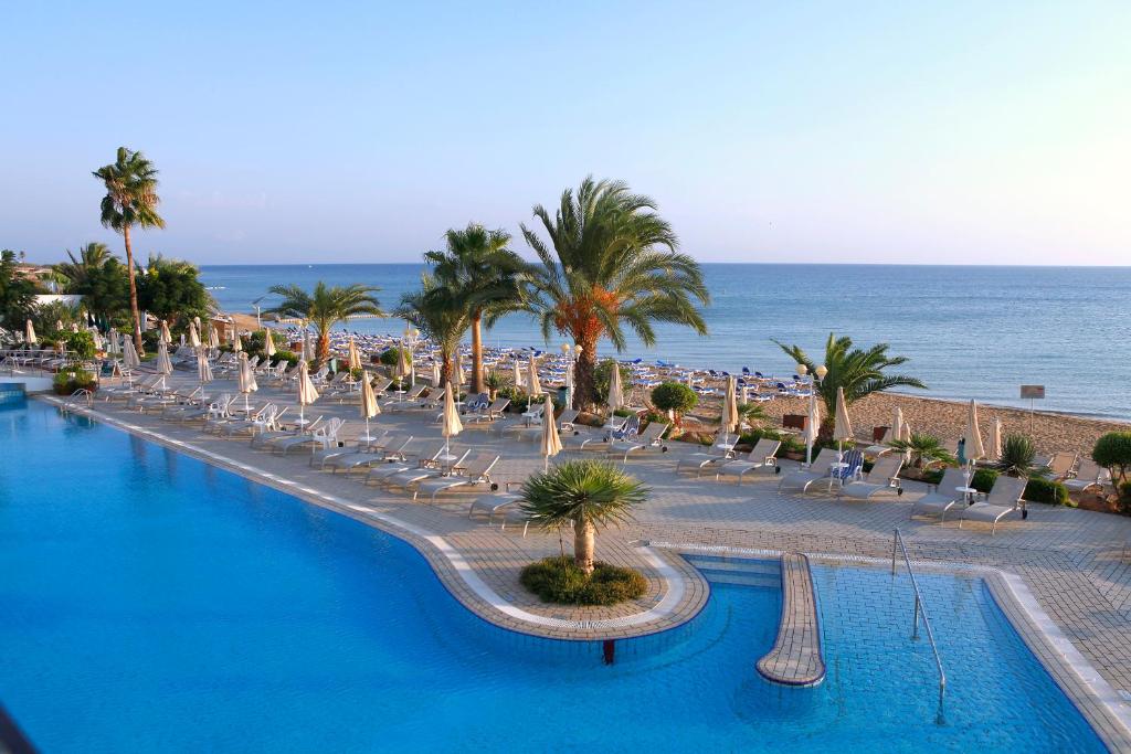 a swimming pool with chairs and palm trees and the ocean at Sunrise Beach Hotel in Protaras