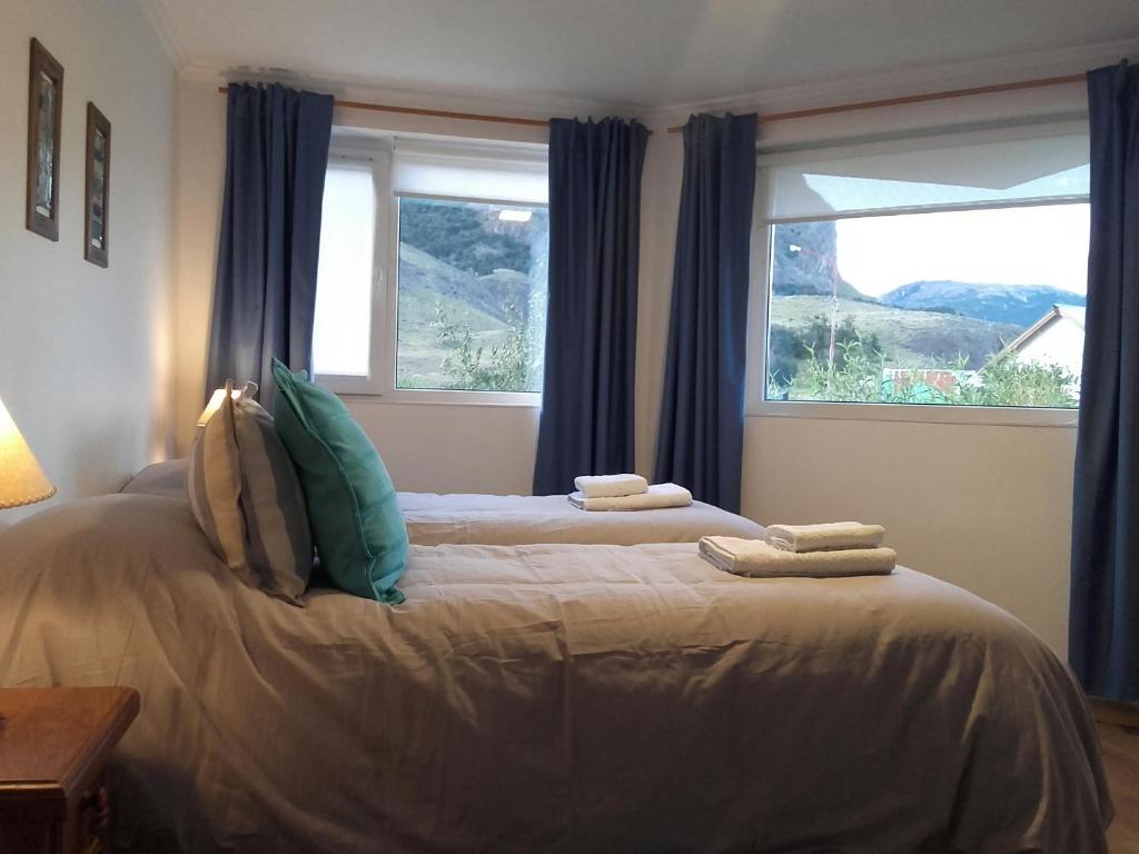a bedroom with a bed with blue curtains and two windows at Los Coirones Aparts - El Chaltén - Patagonia in El Chalten