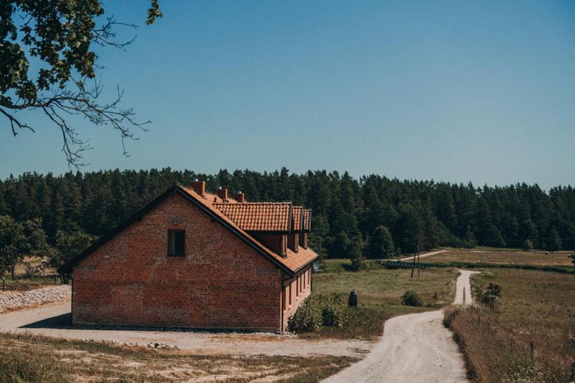a brick building in a field next to a dirt road at Apartamenty Rodzinne in Wojciechy