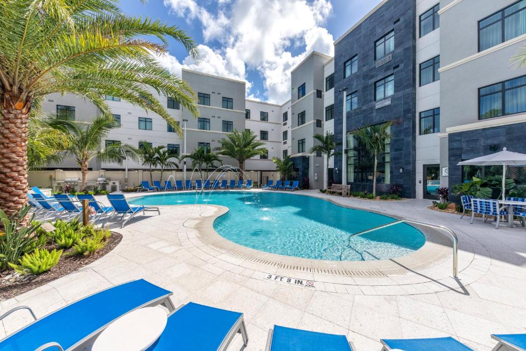 a pool with blue chairs and palm trees in front of a building at Staybridge Suites - Naples - Marco Island by IHG in Naples