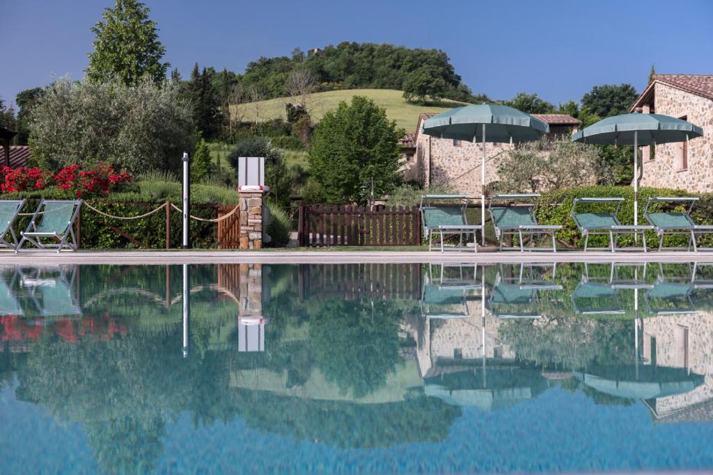 a pool of water with chairs and umbrellas at Antica Fonte Resort in Casole dʼElsa