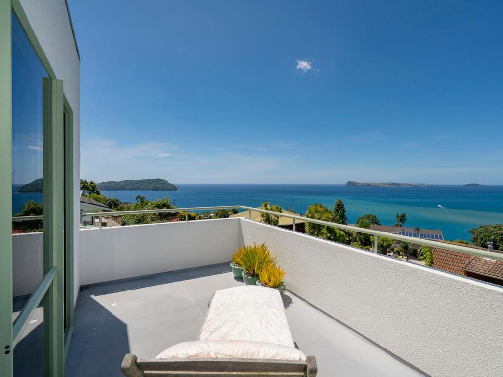 a balcony with a bench and a view of the ocean at Picturesque on Paku - Tairua Holiday Home in Tairua