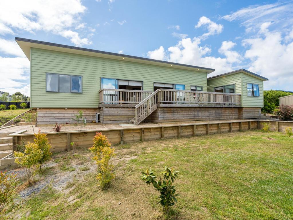 una casa verde con un ampio ponte su un prato di Driftwood Views - Mangawhai Heads Holiday Home a Mangawhai