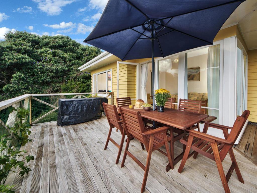 ピハにあるSurfer's Sunshine Cottage - Piha Holiday Homeの木製テーブル、椅子、パラソル付きのデッキ