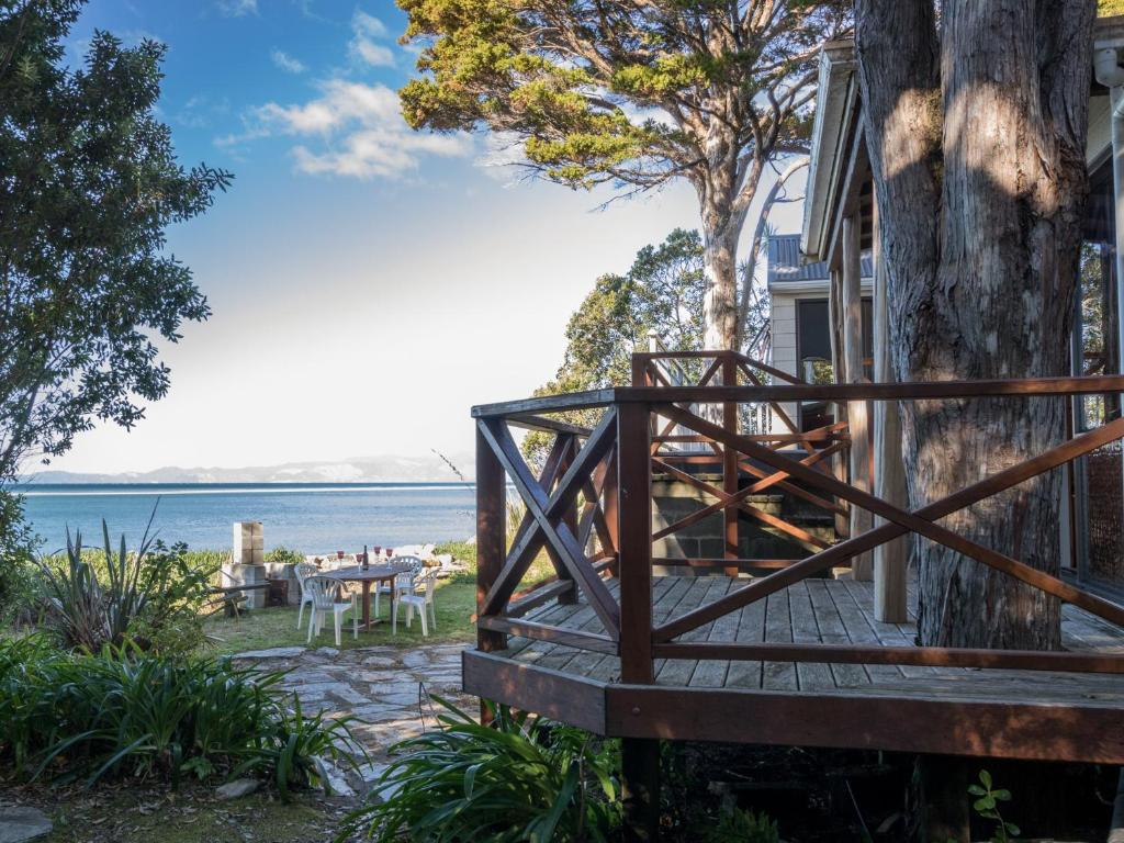 a house with a wooden deck next to a tree at Matai Cottage - Pakawau Bach in Pakawau