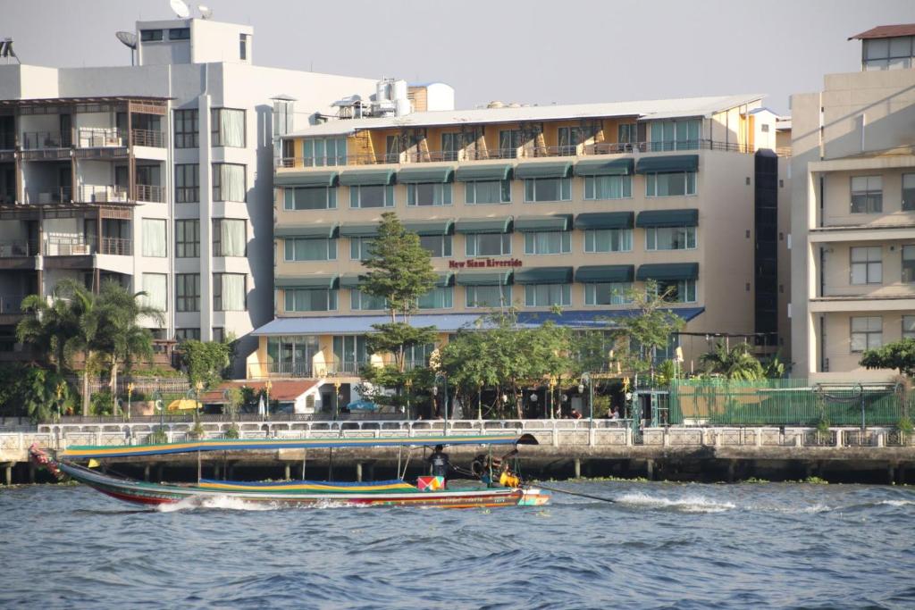 een boot in het water voor gebouwen bij New Siam Riverside - SHA Certified in Bangkok