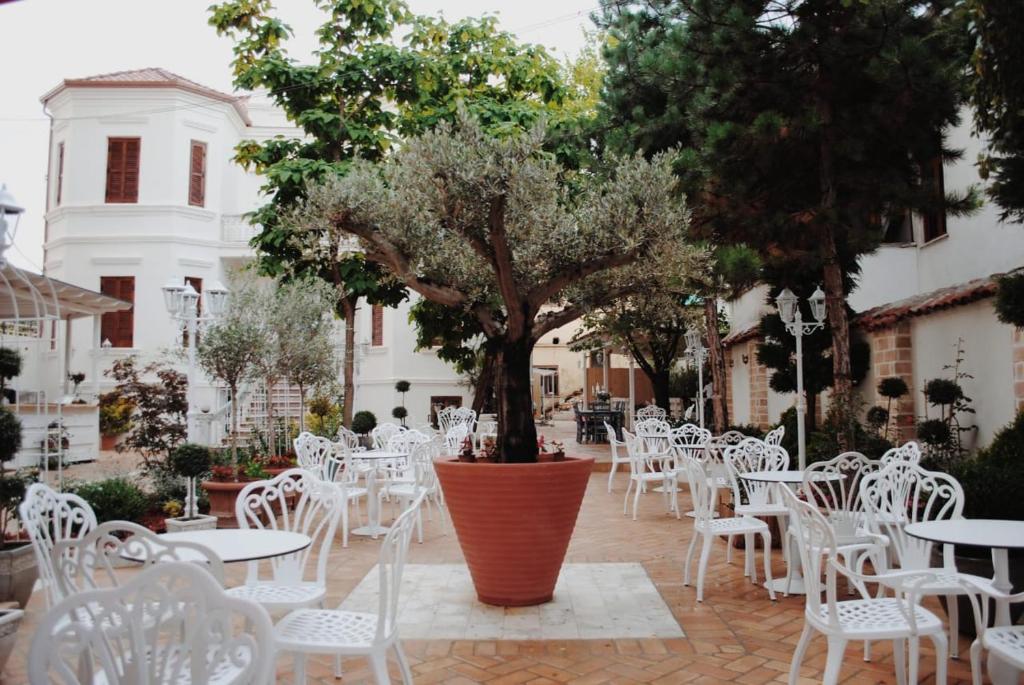 um pátio com mesas e cadeiras brancas e uma árvore em Seven cafe & hotel em Pogradec