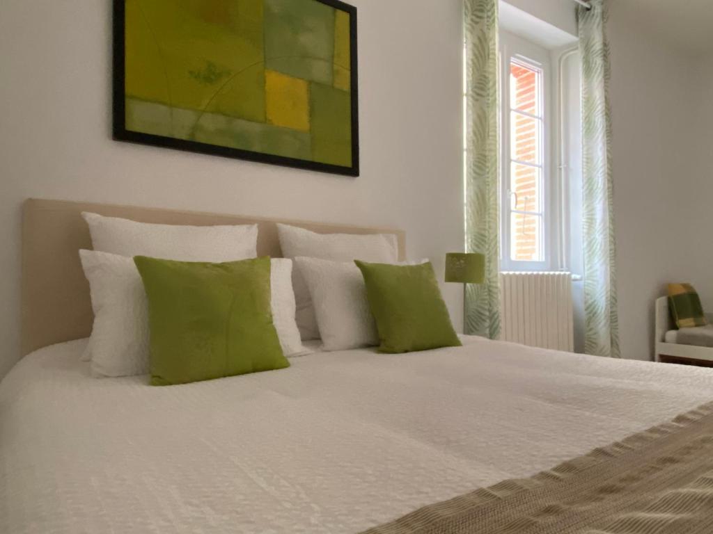 a bedroom with a white bed with green pillows at Gîte tout Confort au Coeur du Village Verniolle in Verniolle