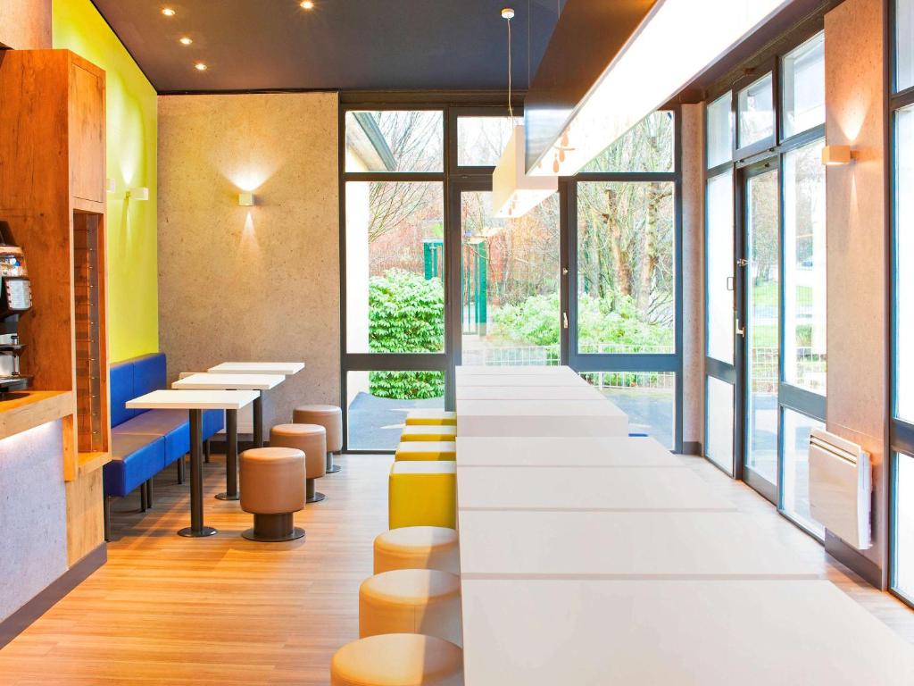 a row of tables and stools in a restaurant with windows at ibis budget Marne la Vallée Bry sur Marne in Bry-sur-Marne