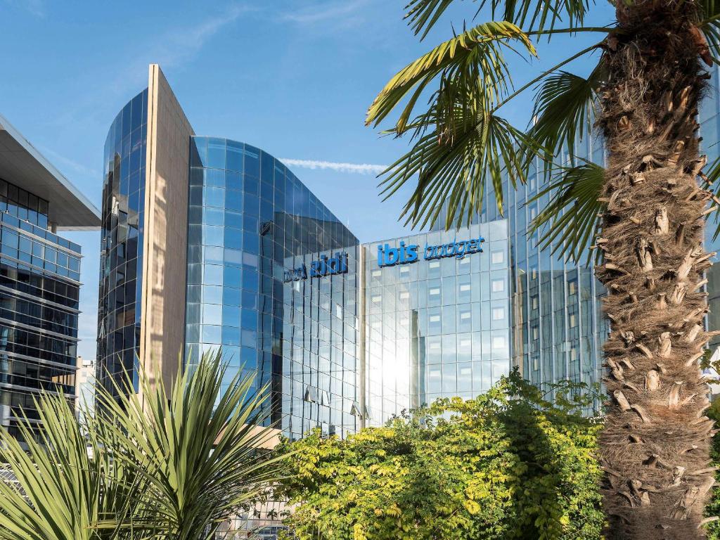 un grand bâtiment en verre avec un palmier devant lui dans l'établissement ibis budget Nice Aeroport, à Nice