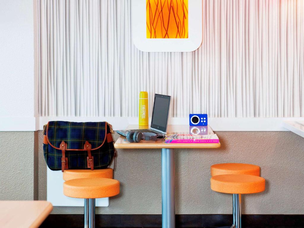 uma secretária com um computador portátil e 2 cadeiras cor-de-laranja em ibis budget Orgeval em Orgeval