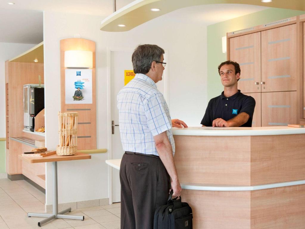 two men standing at a counter in a store at ibis budget Besançon Ecole Valentin in Besançon