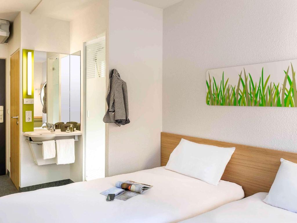 a bedroom with two beds and a sink and a mirror at Ibis Budget Roanne Hôtel in Roanne
