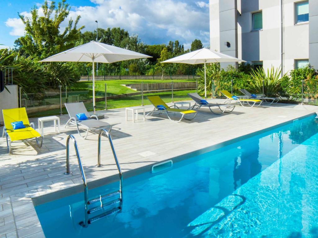 a swimming pool with chairs and umbrellas next to a building at Ibis Budget Valence Sud in Valence