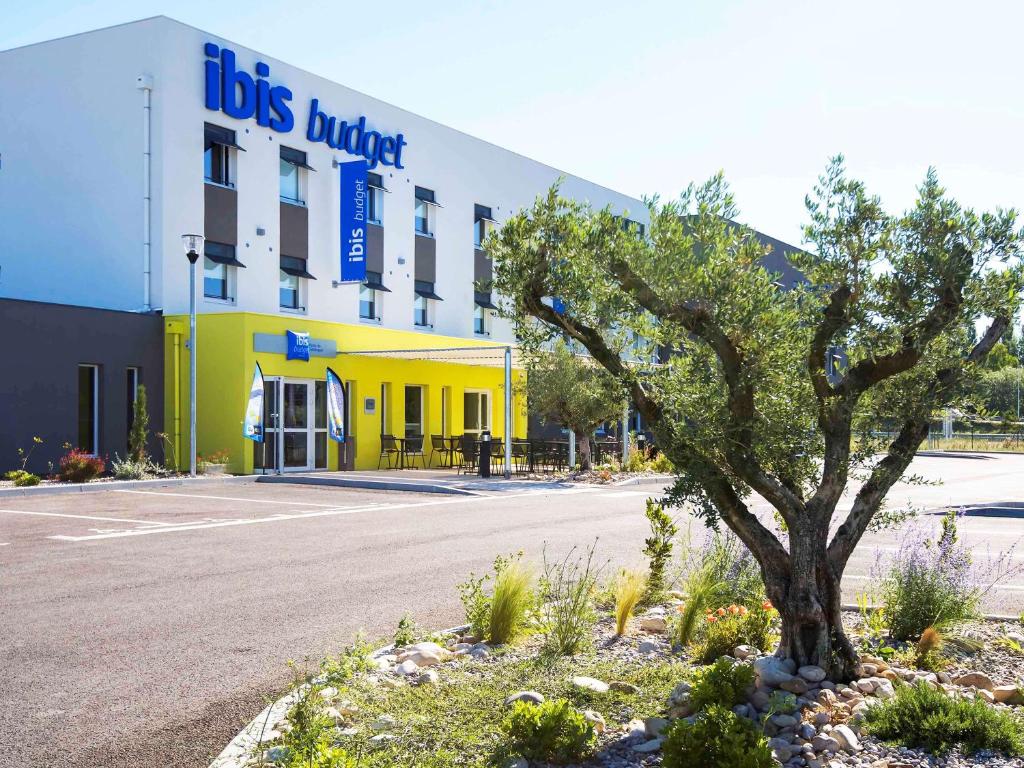 un bâtiment jaune avec un arbre devant lui dans l'établissement Ibis Budget Porte de Camargue, à Saint-Martin-de-Crau