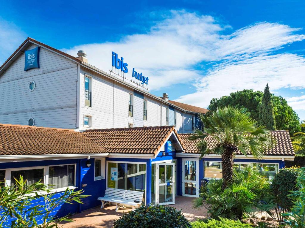 a blue and white hotel with a bench in front of it at Ibis Budget Béziers Est La Giniesse in Béziers