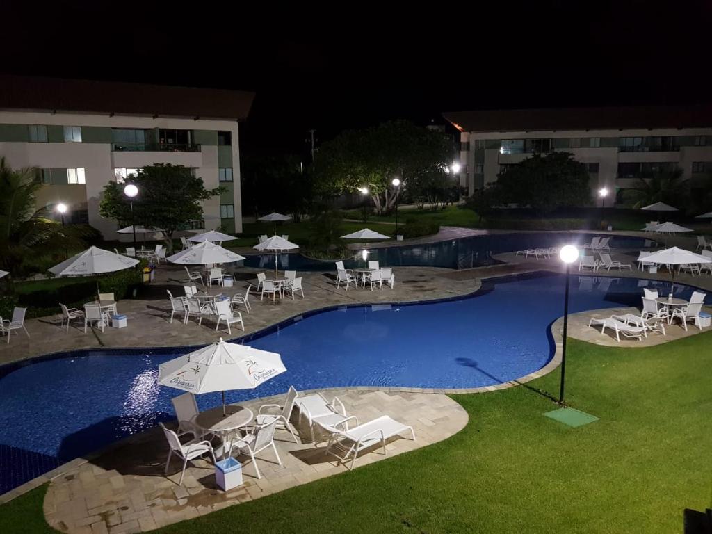 a swimming pool with chairs and umbrellas at night at Carneiros Beach Resort Tamandaré Flat in Tamandaré