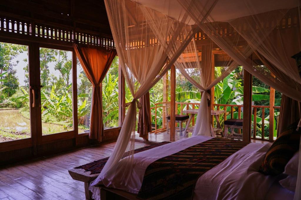 a bedroom with a bed with drapes and windows at Kidem Ubud Villas in Ubud
