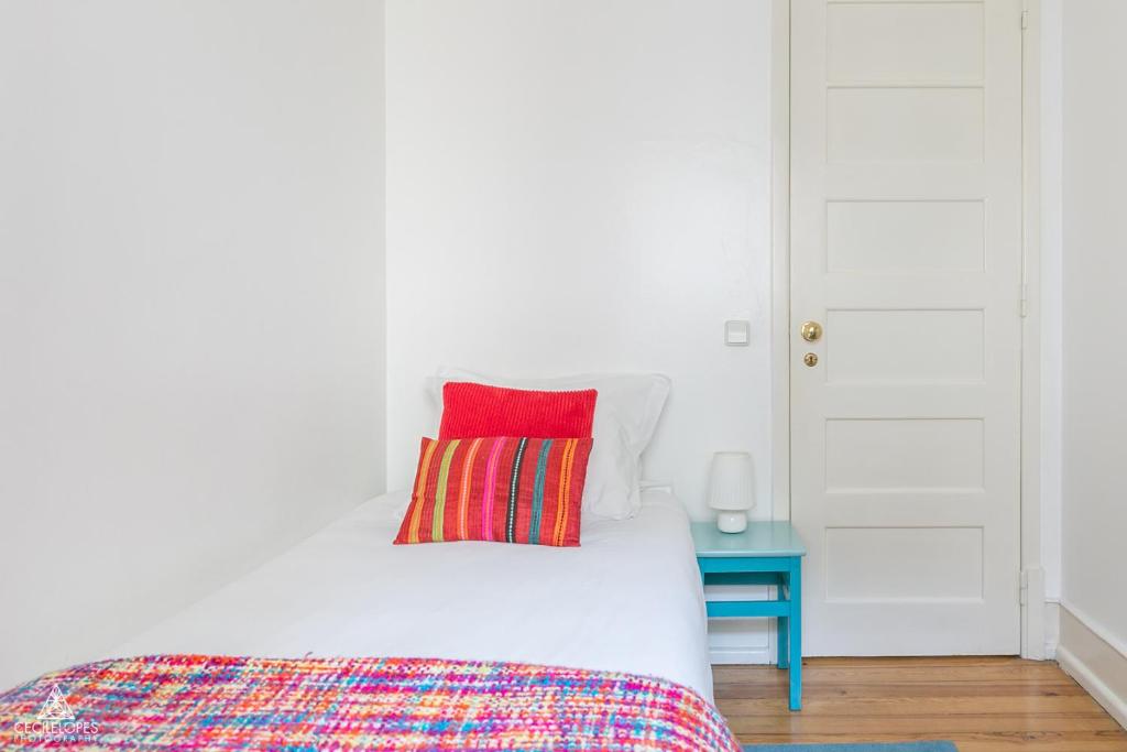 a white bed with a red pillow and a blue table at Casa da Avenida Lisboa in Lisbon